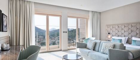 A modern hotel room with a large sliding glass door leading to a balcony, a sofa, a small round table, and a bed with a unique headboard.