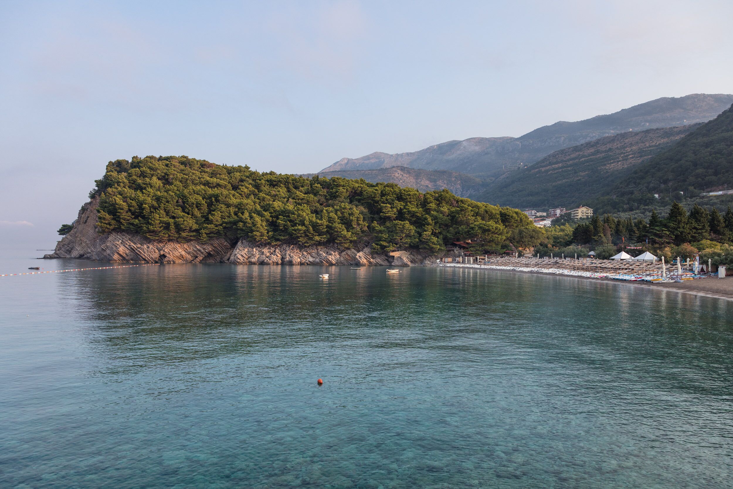 A coastal landscape with a small island, clear water, and distant mountains.