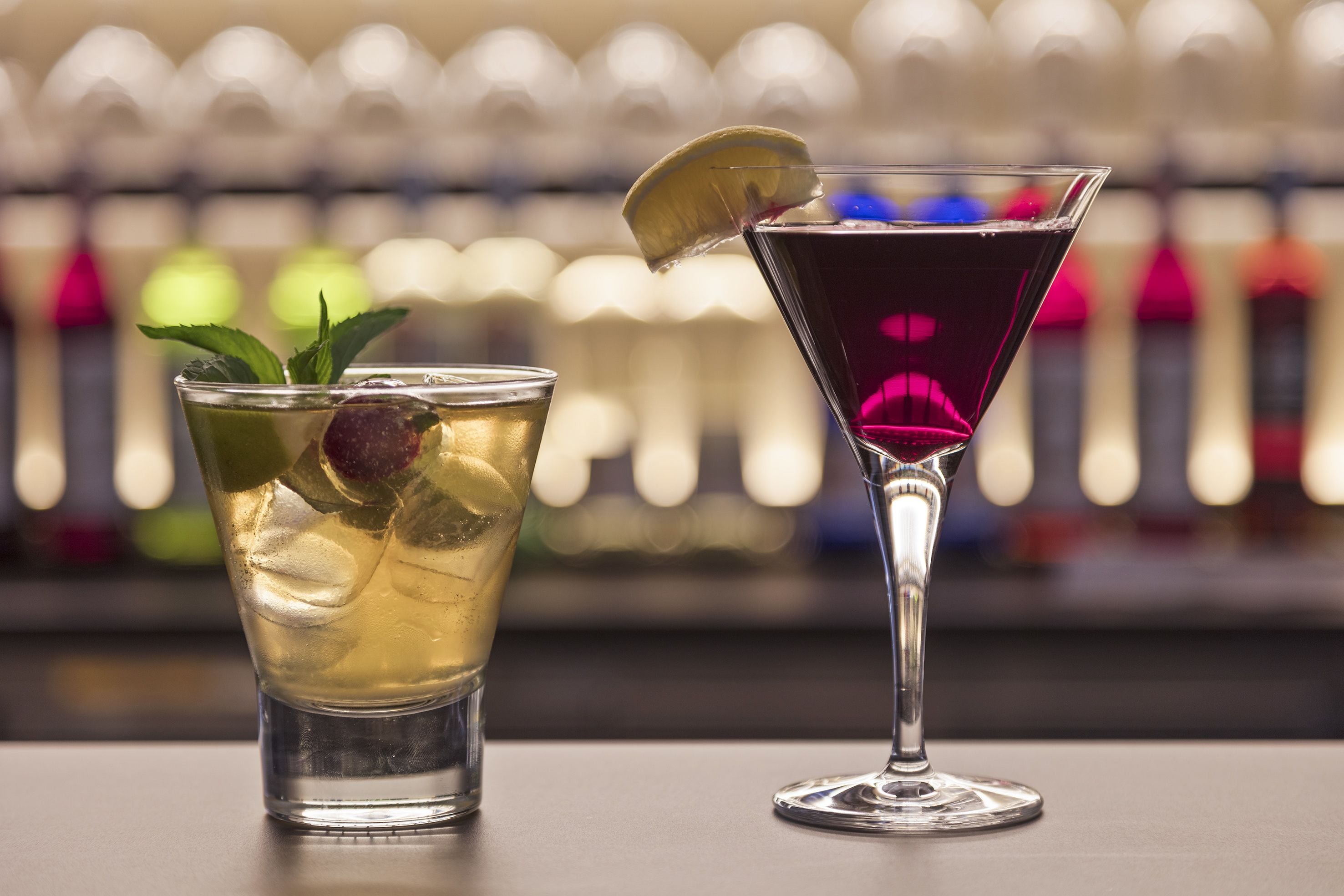 Two glasses of beverages on a bar counter.