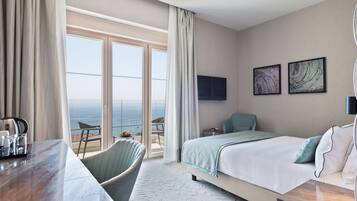 Quarto de hotel com cama, escrivaninha, cadeira, televisão e varanda com vista para o mar.
