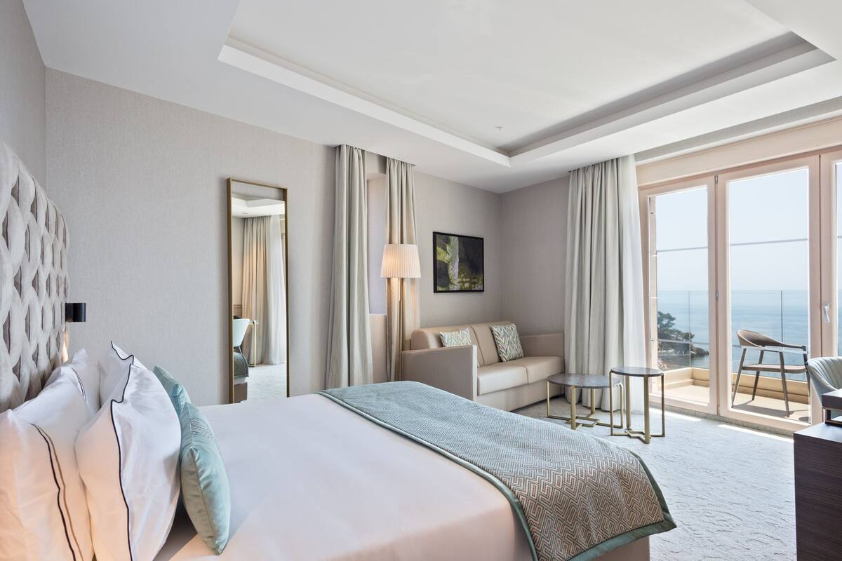 Una habitación de hotel con una cama grande, un sofá, una mesita y un balcón con vistas.