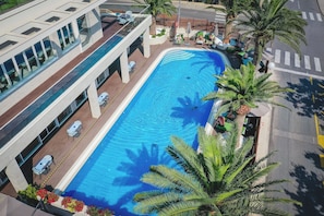 A modern hotel with a swimming pool, outdoor seating, and palm trees.