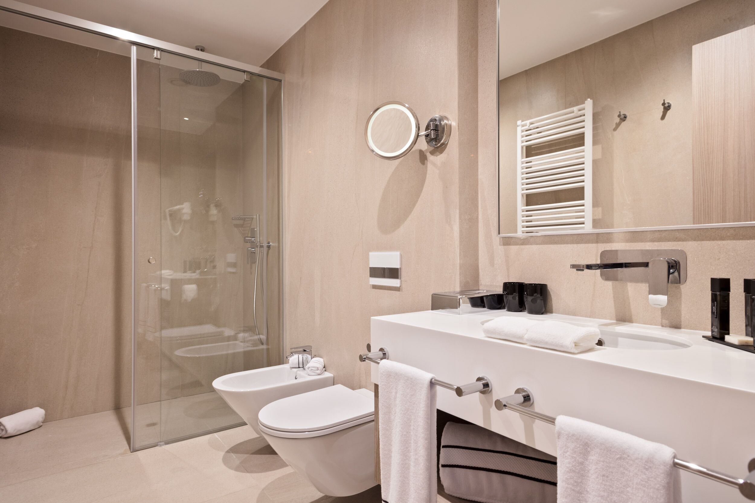 A modern bathroom with a glass shower enclosure, a white bathtub, a toilet, and a large mirror with a towel rack.