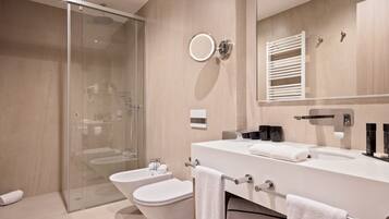 A modern bathroom with a glass shower enclosure, a white bathtub, a toilet, and a large mirror with a towel rack.