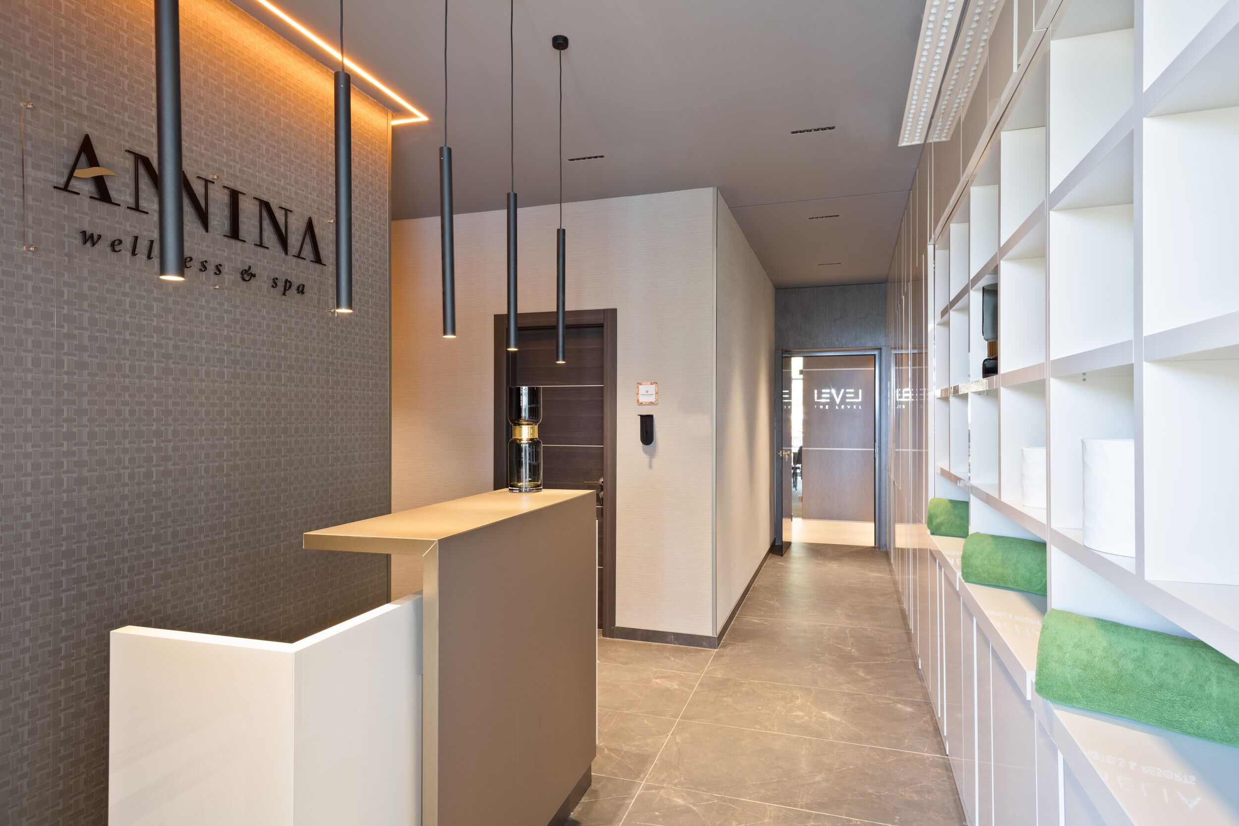 A reception area with a modern design, featuring a reception desk, pendant lighting, and a wall with the name 'ANNINA' indicating a wellness spa.