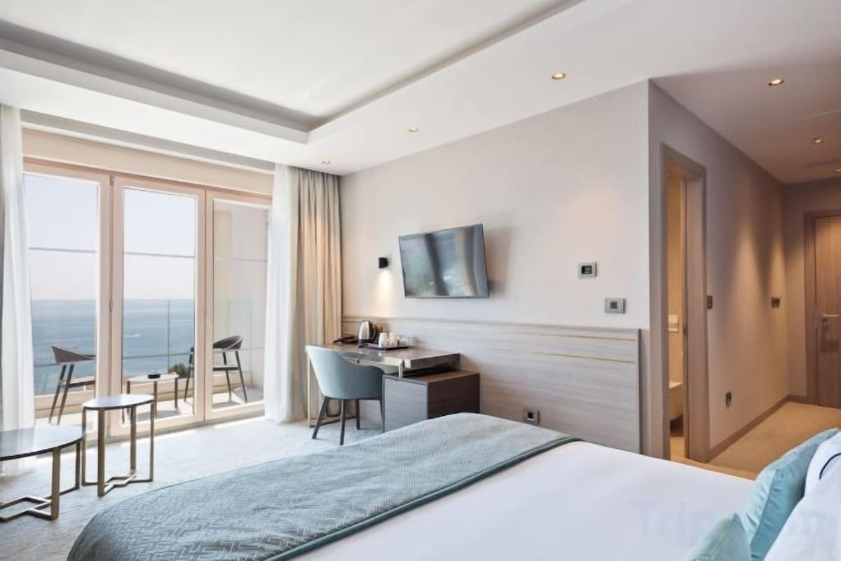 Une chambre d’hôtel équipée d’un lit, d’un bureau, de chaises, d’une télévision et d’un balcon avec vue.