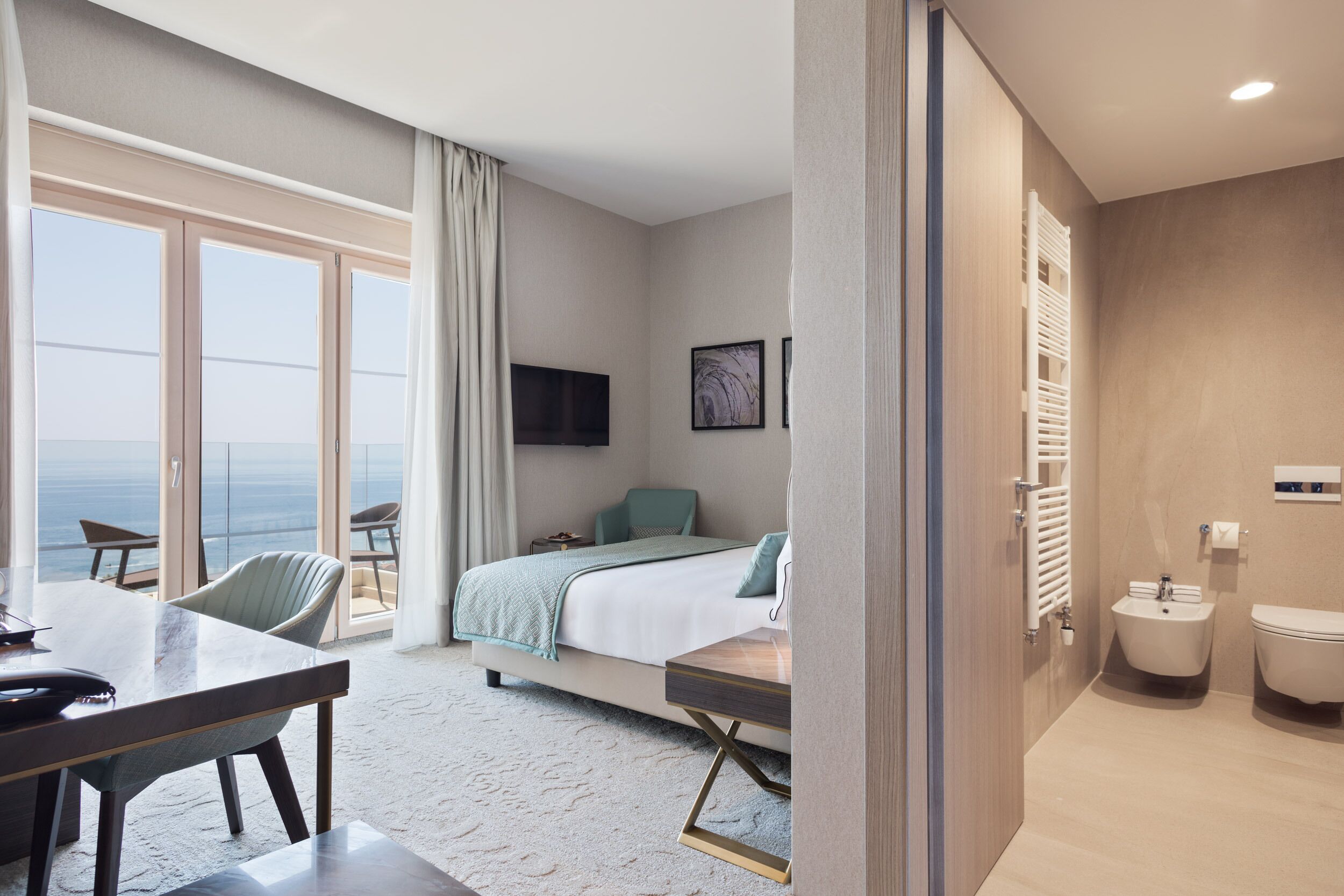 A hotel room with a bed, a desk, a chair, a TV, a window with a view, and a bathroom.