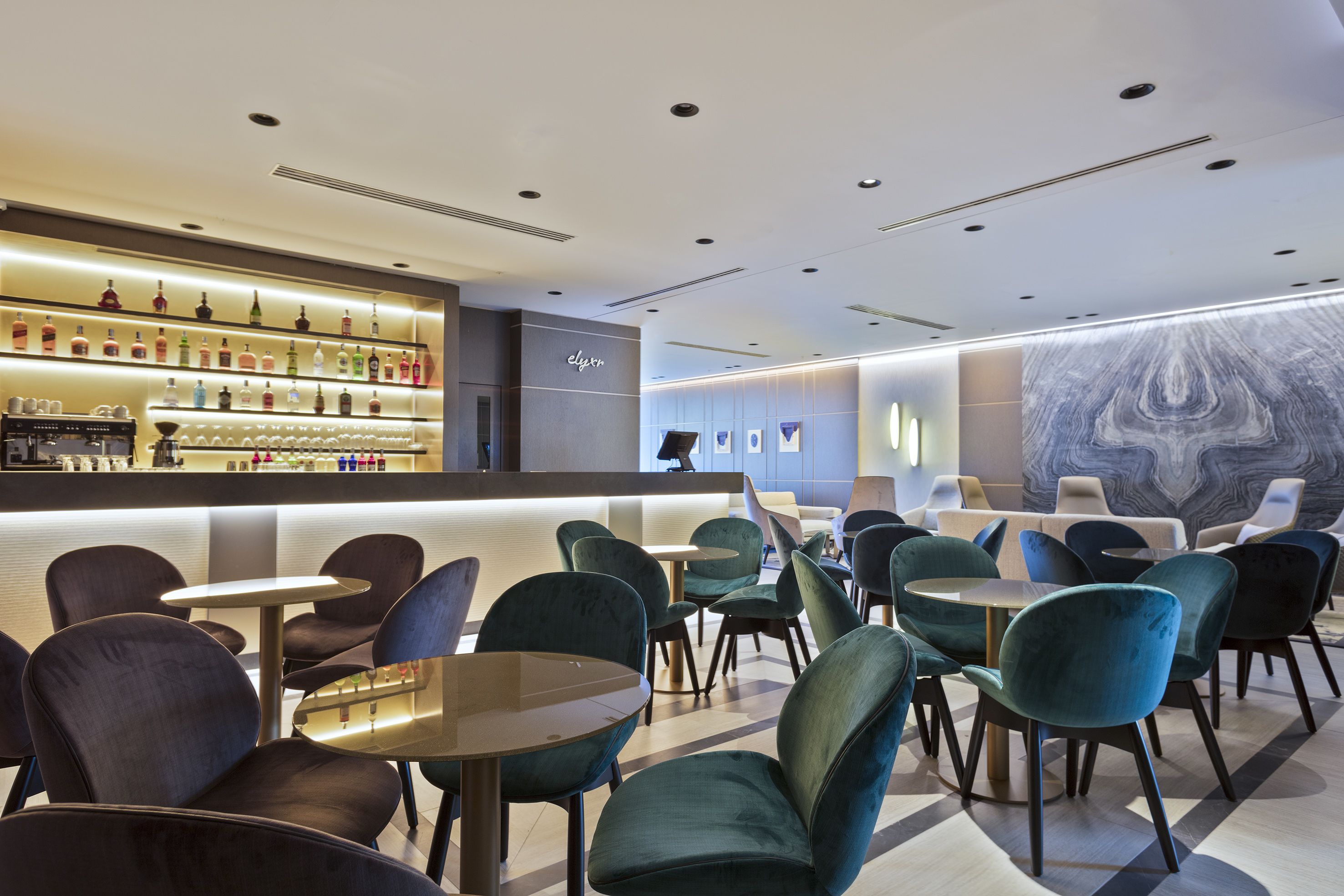 Zona de bar moderna con una variedad de botellas de licor y un área de estar con mesas y sillas redondas.