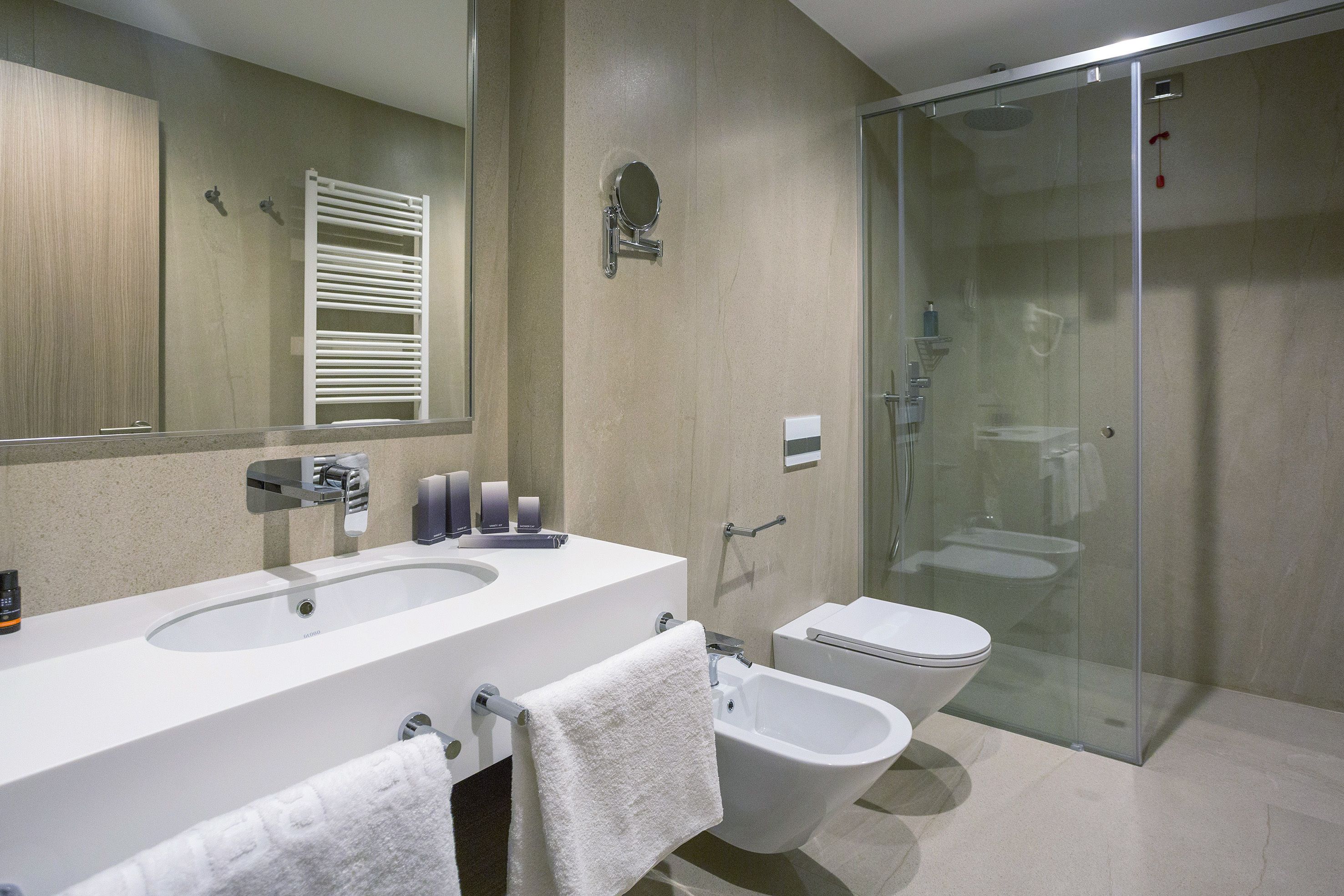 A modern bathroom with a double sink, a bidet, a glass-enclosed shower, and a large mirror.