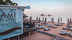 Een strandgebied met een rij ligbedden en parasols, een klein steigertje met een boot, en een bord voor een hotel, spa en congresfaciliteit.