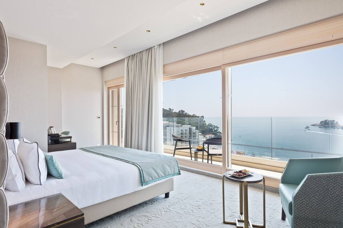 Habitación de hotel moderna con una cama grande, una mesita, un sofá y un balcón con vistas al mar.