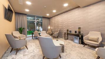 Un espacio lounge moderno con diversas opciones de asientos, un amplio ventanal que proporciona luz natural y una pared con textura.