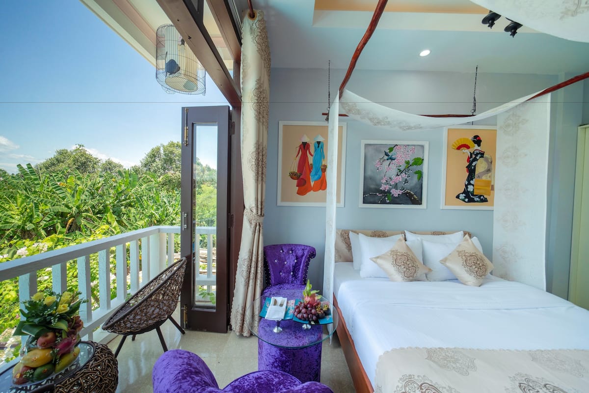 A bedroom with a bed, a chair, a table with fruit, and a balcony with plants.