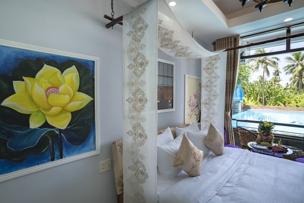 A bedroom with a large bed, a window with a view of palm trees, and a painting of a lotus flower.