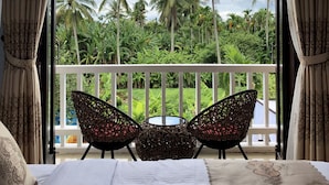 A bedroom with a balcony, a bed, two wicker chairs, and a view of palm trees and greenery. - VIP Garden Villa and Pool (Da Nang)