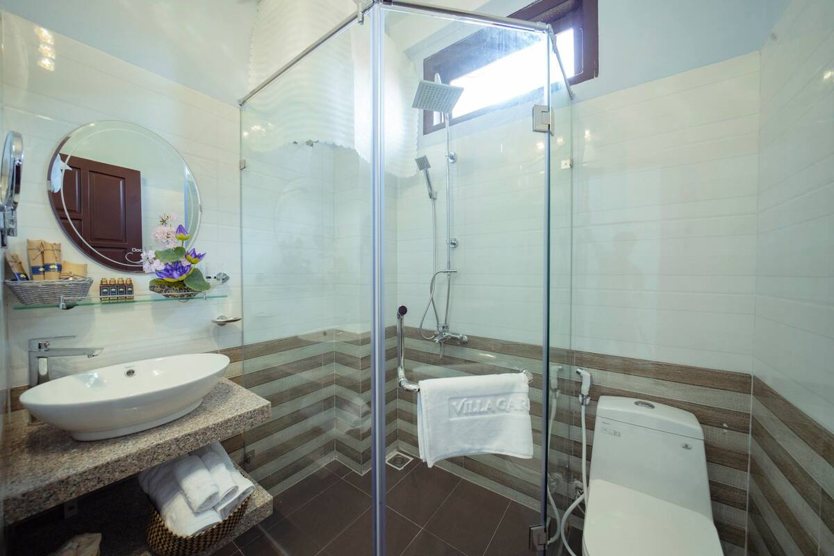 A bathroom with a glass-enclosed shower, a round mirror, a sink, and a towel rack.