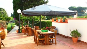An outdoor patio with a wooden table and chairs, surrounded by potted plants and a large umbrella. - B&B Verdegiada (Brindisi)