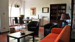 A living room with a checkered floor, a black sofa, a dining table with chairs, and a bookshelf. - B&B Verdegiada (Brindisi)