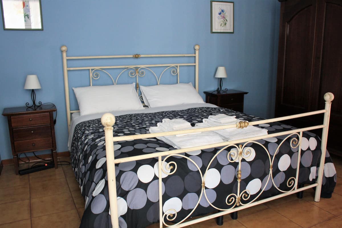 A bed with a metal frame, white bedding, and a black and white polka dot duvet. There are two bedside tables with lamps and a dark wooden wardrobe.