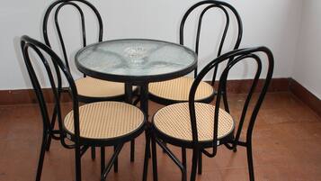 A round glass table with four black metal chairs, each with a woven seat, on a tiled floor.