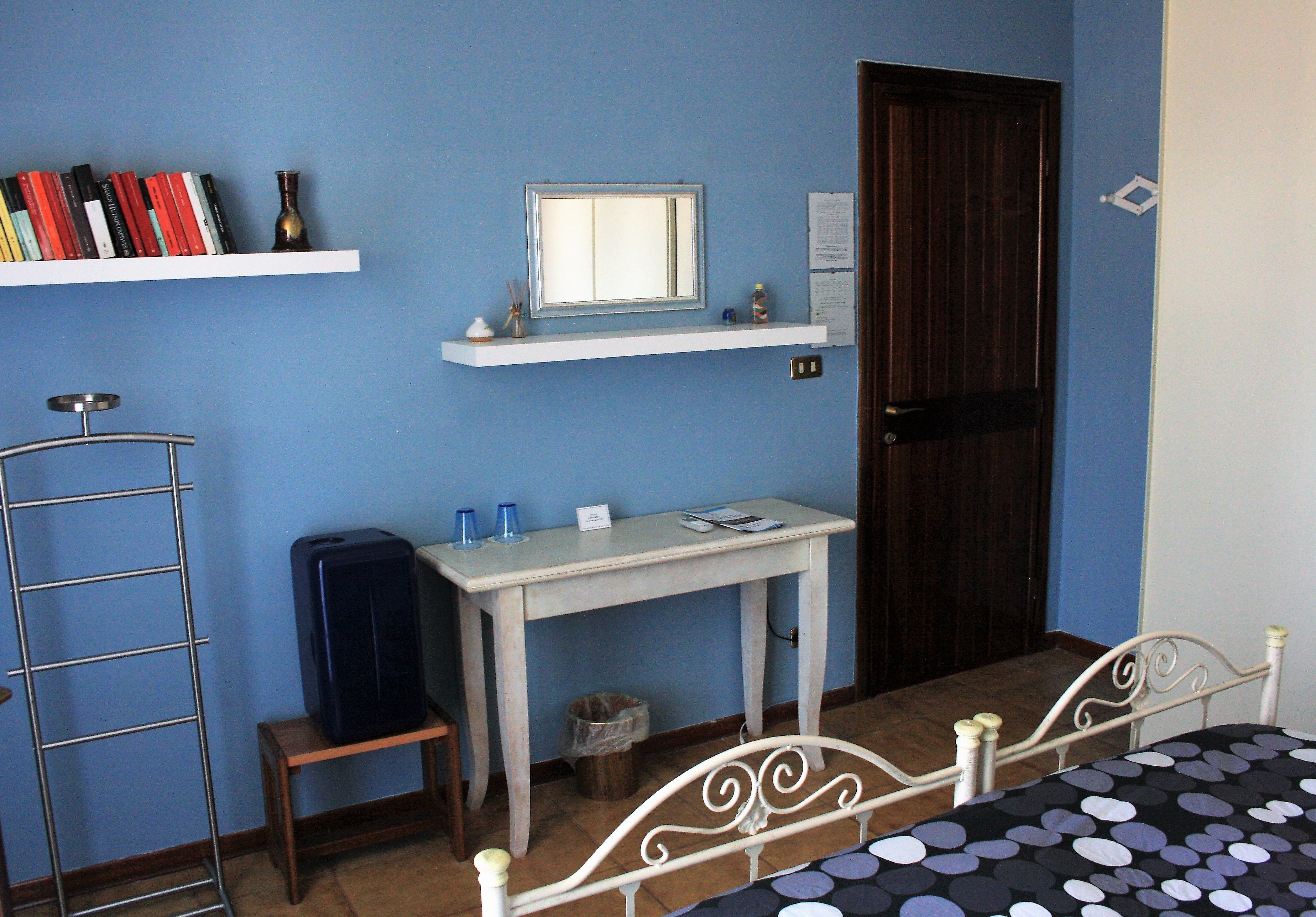 Une chambre à coucher avec un lit, un bureau, une chaise, une étagère avec des livres, un miroir et une porte.