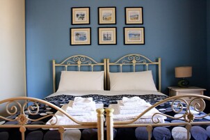 Una cama con estructura metálica, almohadas blancas y una pared azul con cuadros enmarcados.