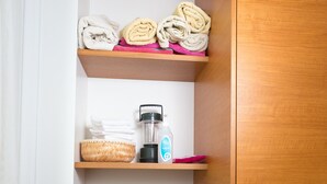 Een badkamer met houten planken waarop handdoeken, een haardroger en een mandje liggen.