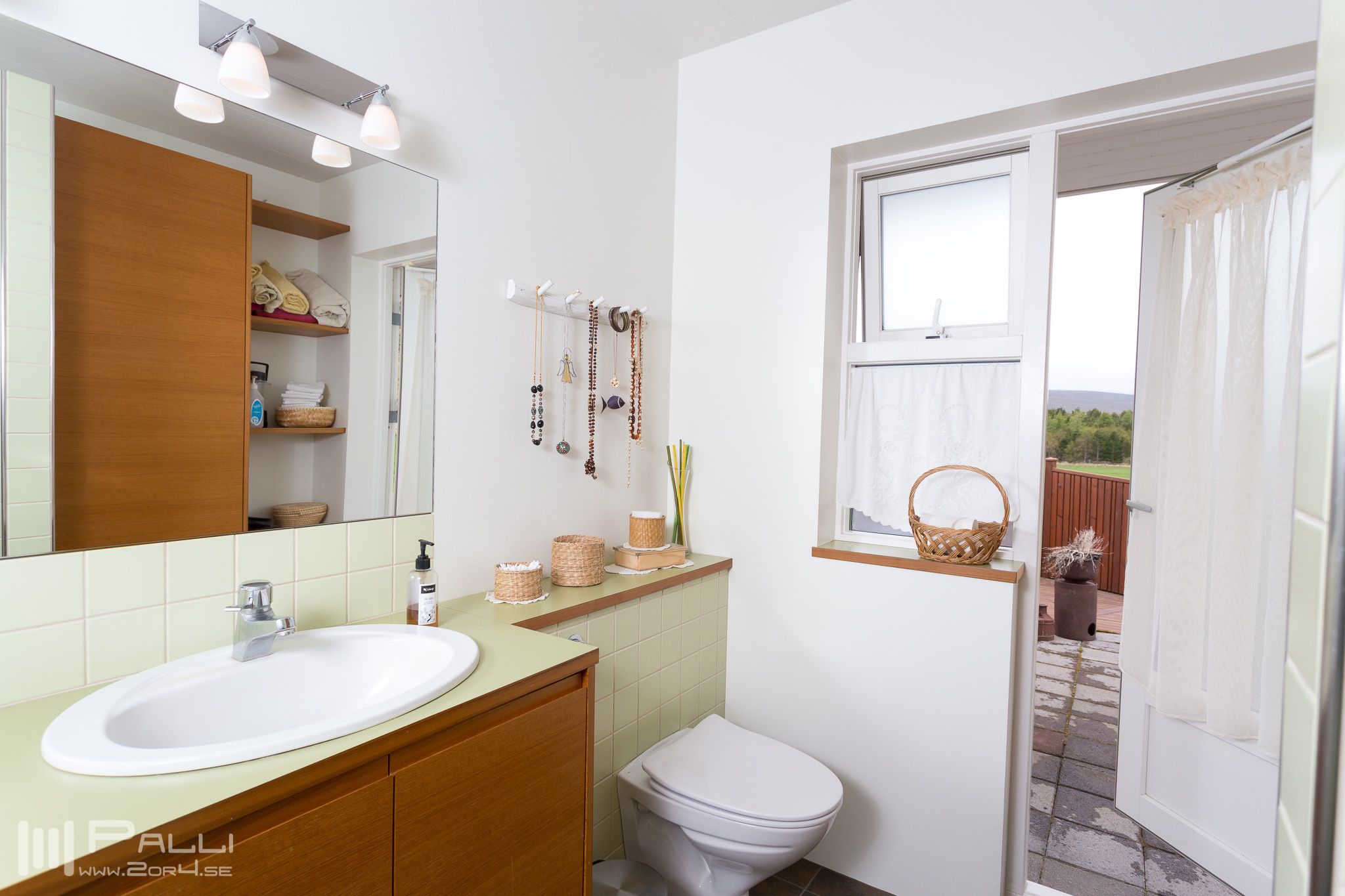A bathroom with a white sink, wooden cabinets, a white toilet, and a window with a view of greenery.