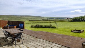 Een buiten terras met een houten tafel en stoelen, een barbecue en uitzicht op glooiende heuvels.