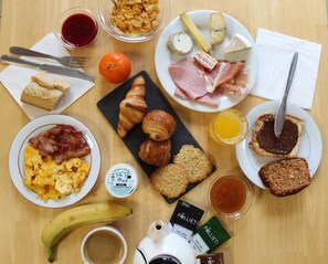 A breakfast table with croissants, cheese, ham, eggs, toast, jam, and a banana. - Hotel Melodie (Bellignat)