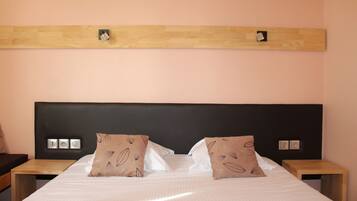 A neatly made bed with a checkered bedspread, two pillows with a leaf pattern, a wooden headboard, and bedside tables with a small clock and a picture frame.