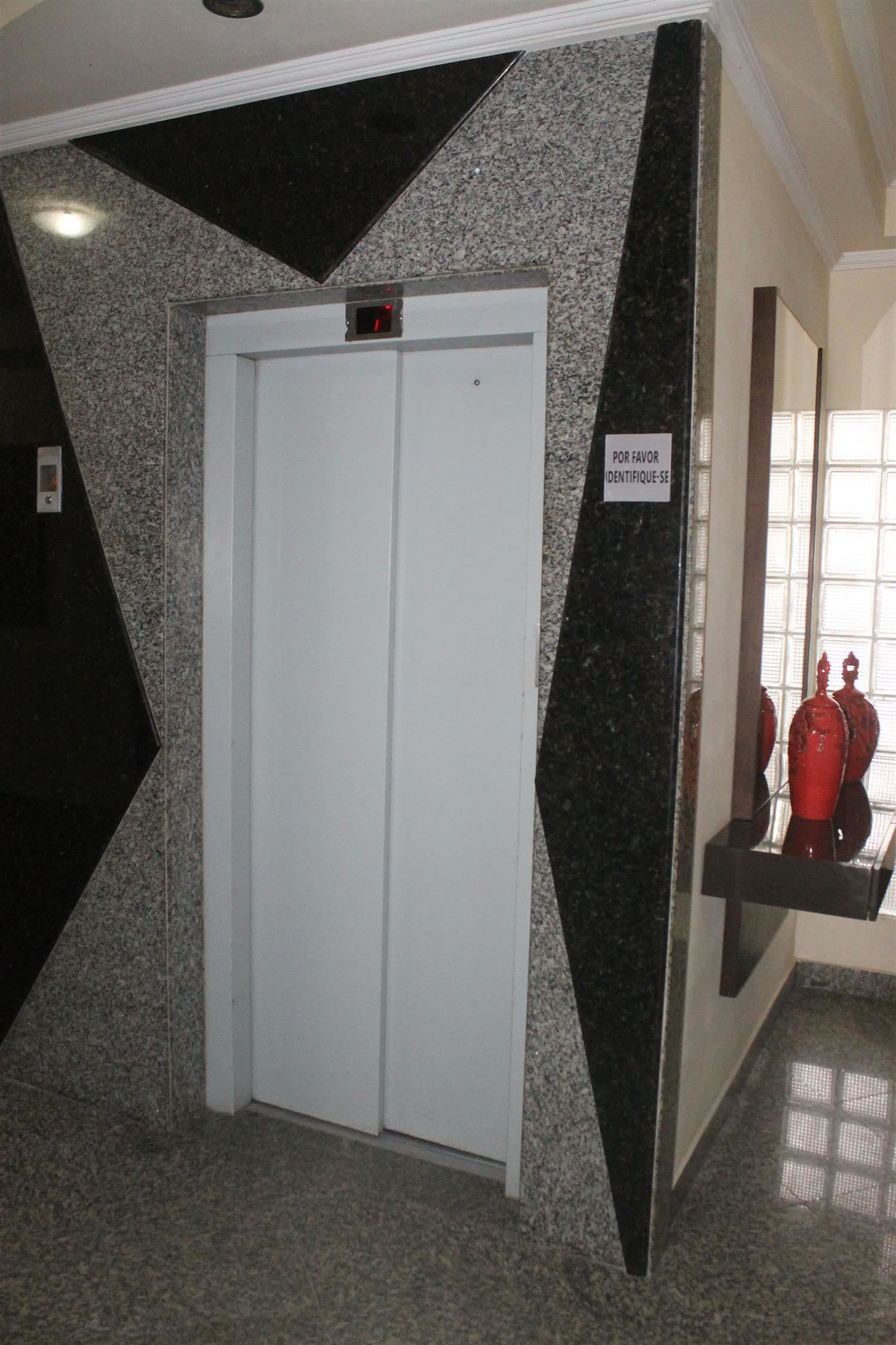 An elevator with a digital display, a sign above it, and a red fire extinguisher to the right.
