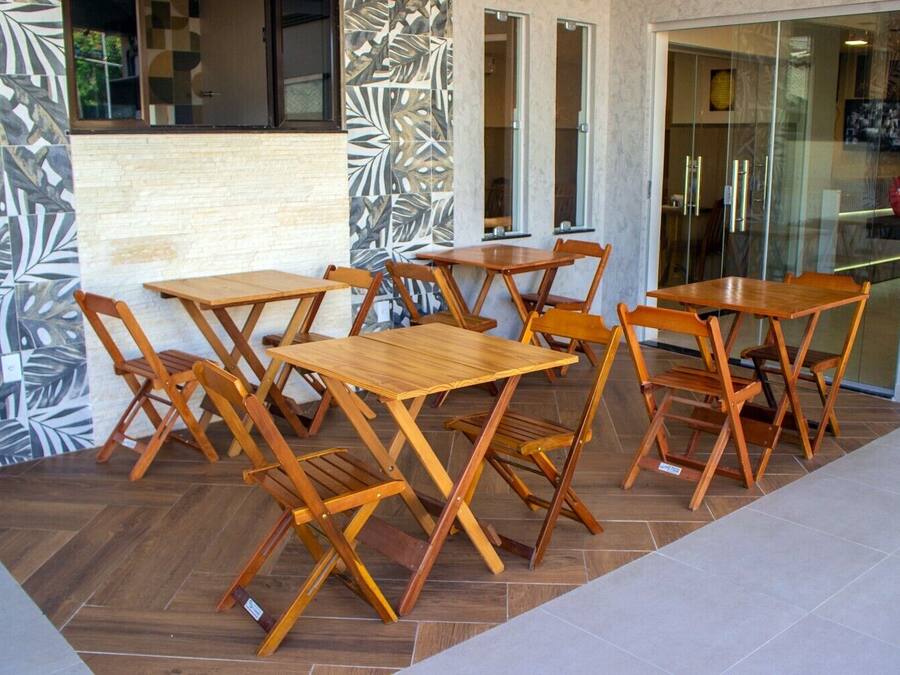 Un espace extérieur aménagé avec des tables et des chaises en bois, un sol carrelé et une porte vitrée donnant accès à l’intérieur.