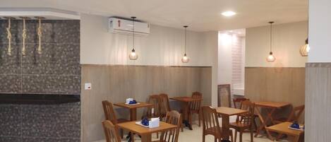 Un restaurante con mesas y sillas de madera, luces colgantes y un equipo de aire acondicionado.