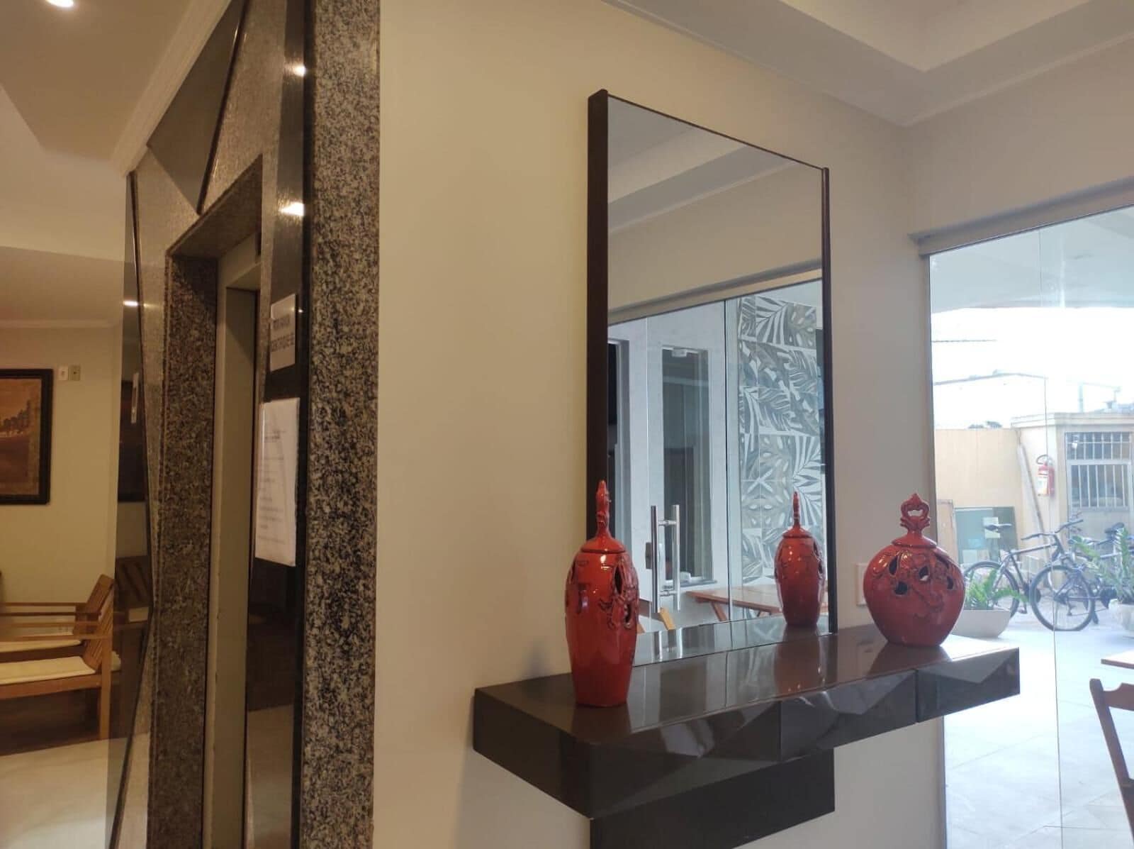 A modern interior with a large mirror reflecting a room with a glass door, a bench, and a bicycle in the background.