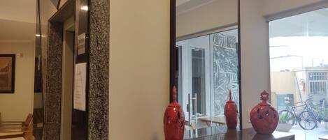 A modern interior with a large mirror reflecting a room with a glass door, a bench, and a bicycle in the background.