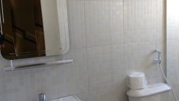Une salle de bain avec un lavabo blanc, un miroir, des toilettes et une poubelle bleue.