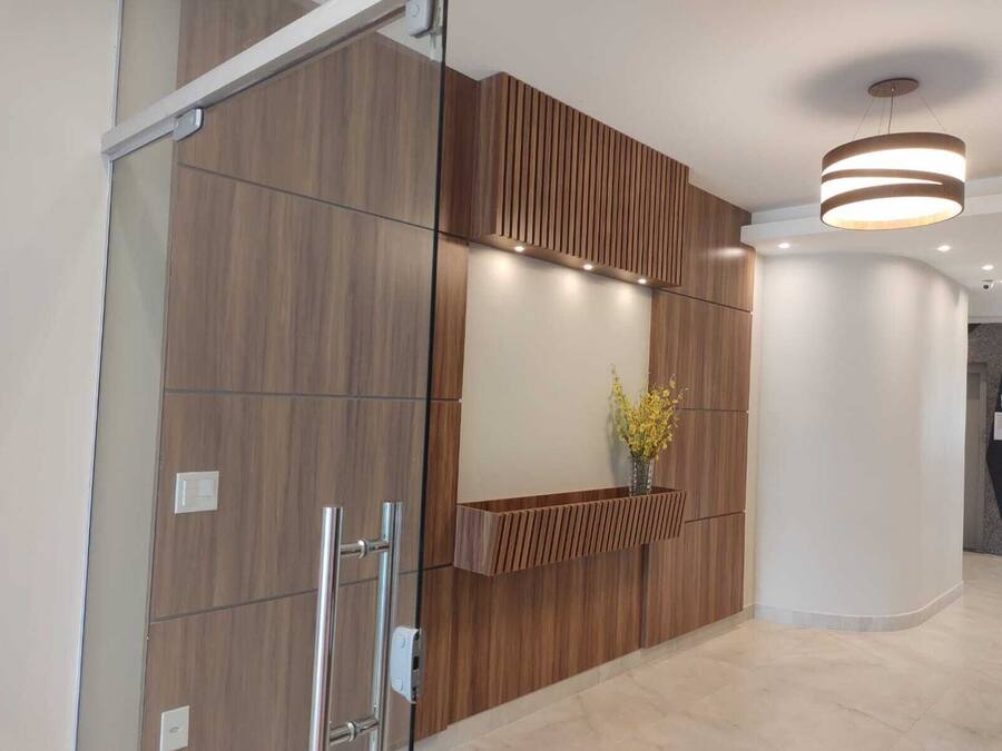 Un área de recepción moderna con paneles de madera, una pared de vidrio y un jarrón con flores amarillas.