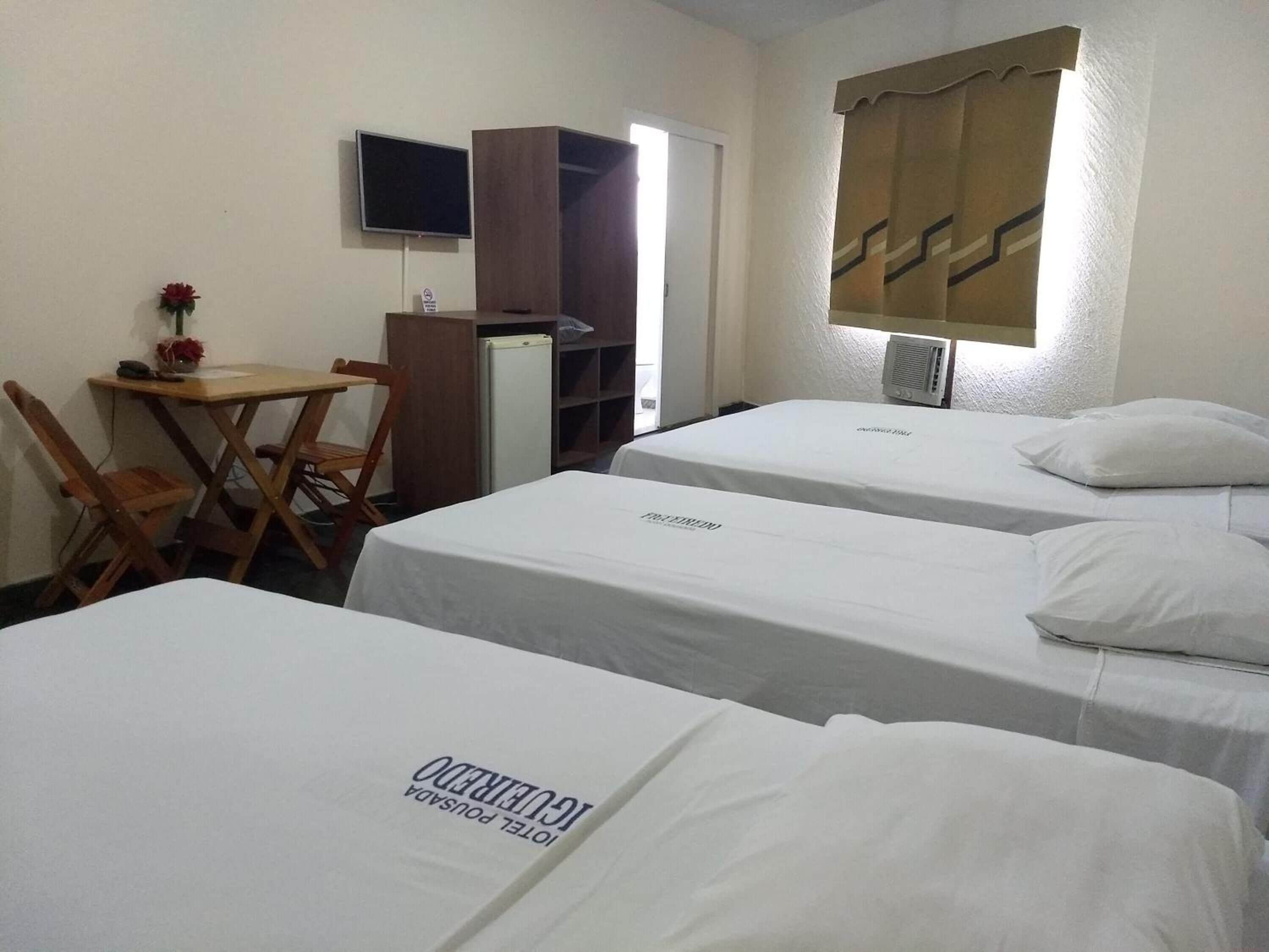 Habitación de hotel con tres camas individuales, un escritorio con silla, televisión y armario.