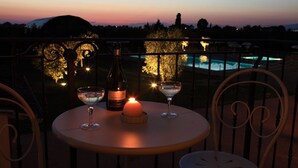 A table with a bottle of wine, two glasses, and a candle on a balcony overlooking a pool. - Agriturismo La Regina (Cascina)