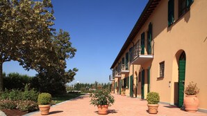 A building with a tiled walkway, green shutters, and potted plants. - Agriturismo La Regina (Cascina)