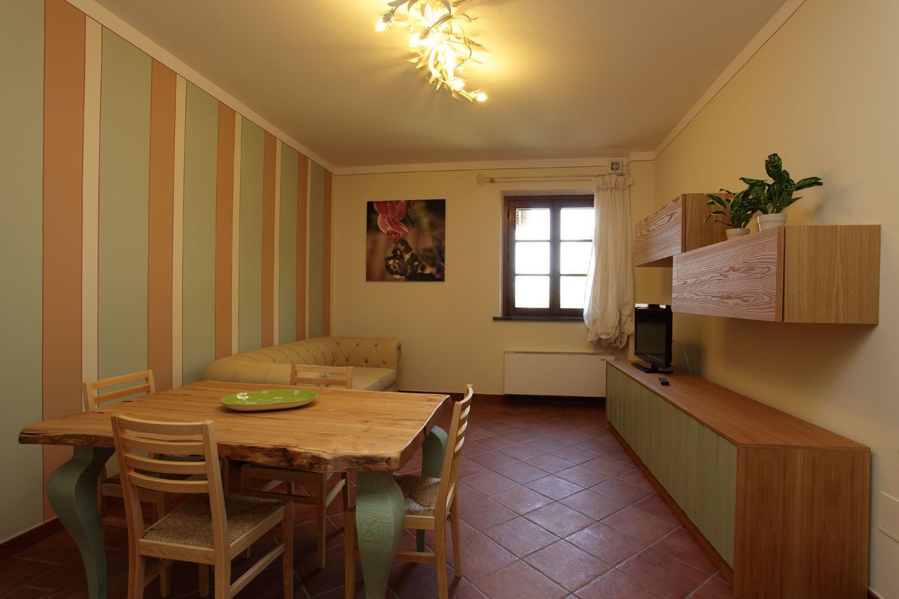 A dining area with a wooden table and chairs, a bench, a television on a wooden cabinet, and a window with curtains.