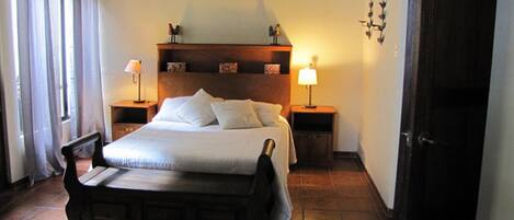 A bedroom with a wooden bed, two bedside tables with lamps, a headboard, and a tiled floor.