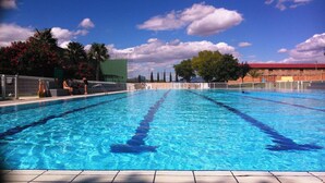 En swimmingpool med klart, blåt vand, omgivet af et hegn, palmer og en bygning med rødt tag.