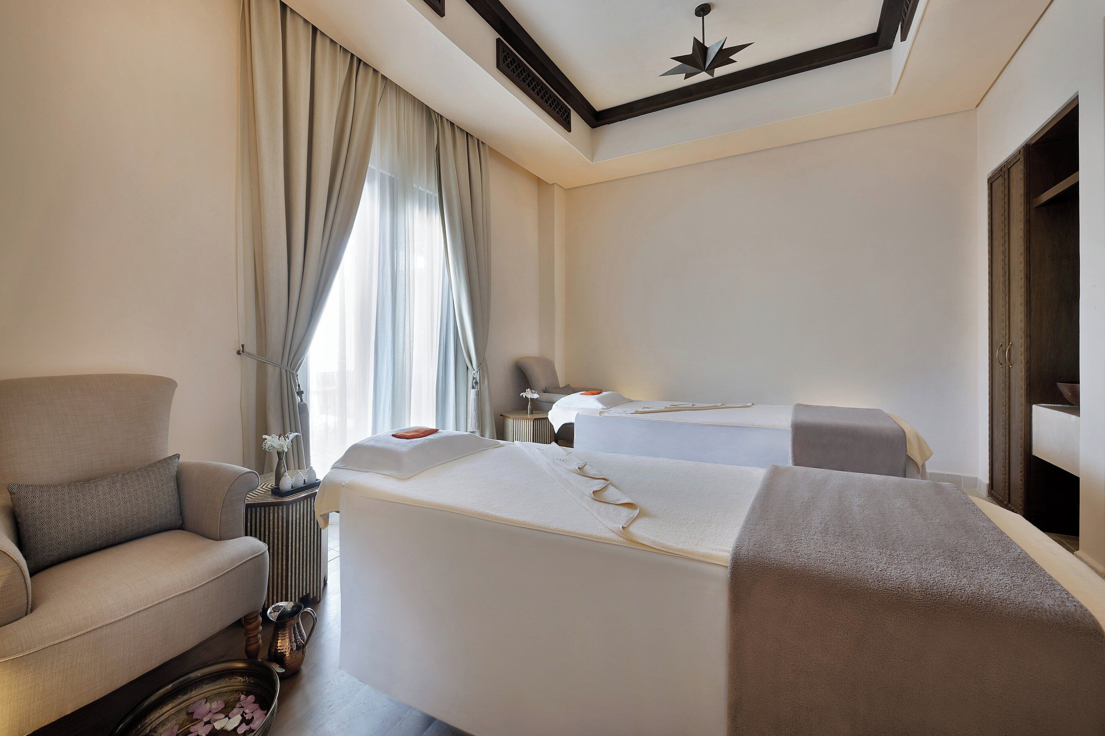 Una habitación de hotel con un sofá, dos camas, una mesita de noche, una ventana con cortinas y un aplique de techo.