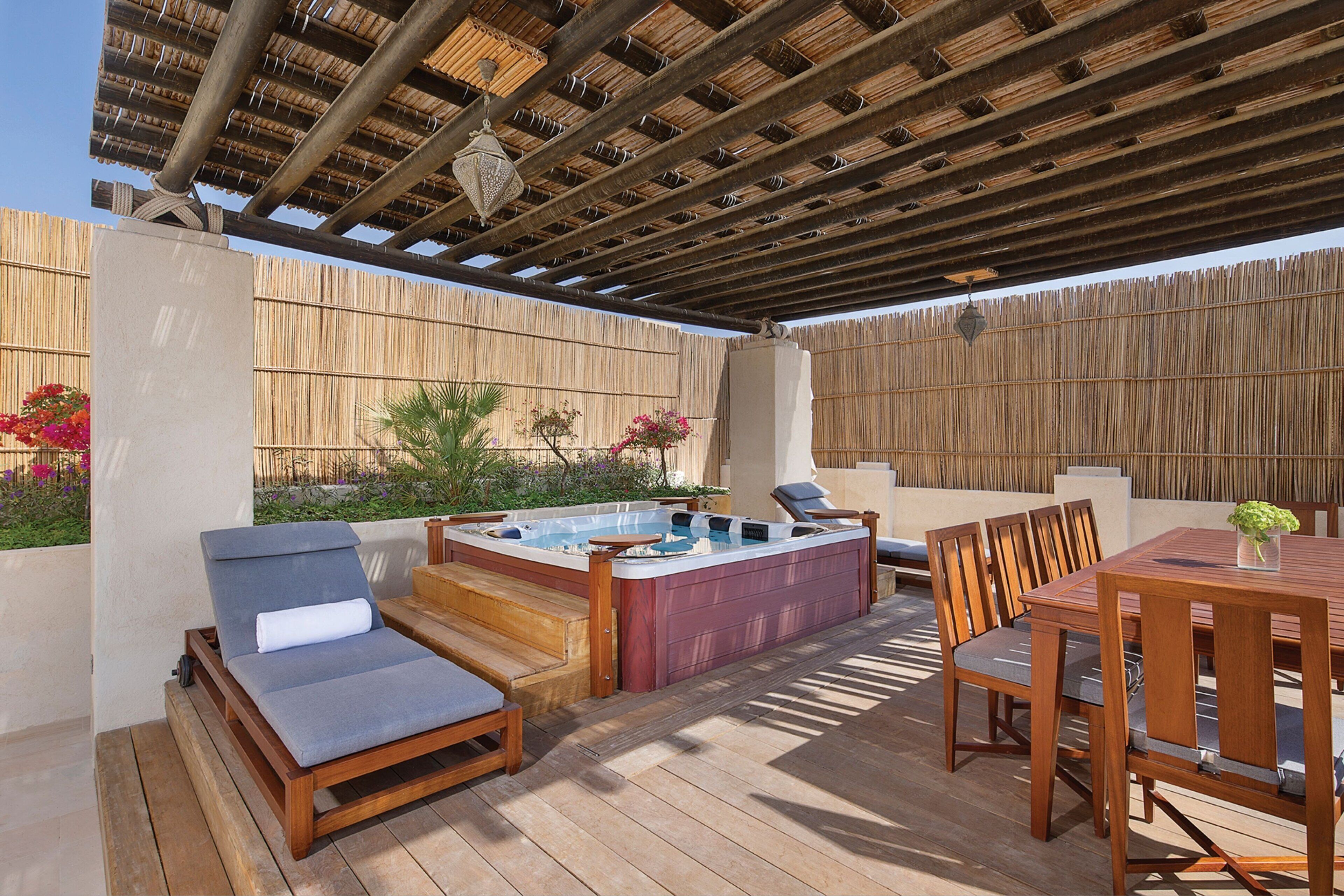 Eine Holzterrasse mit Whirlpool, Liegestühlen und einem Esstisch mit Stühlen.