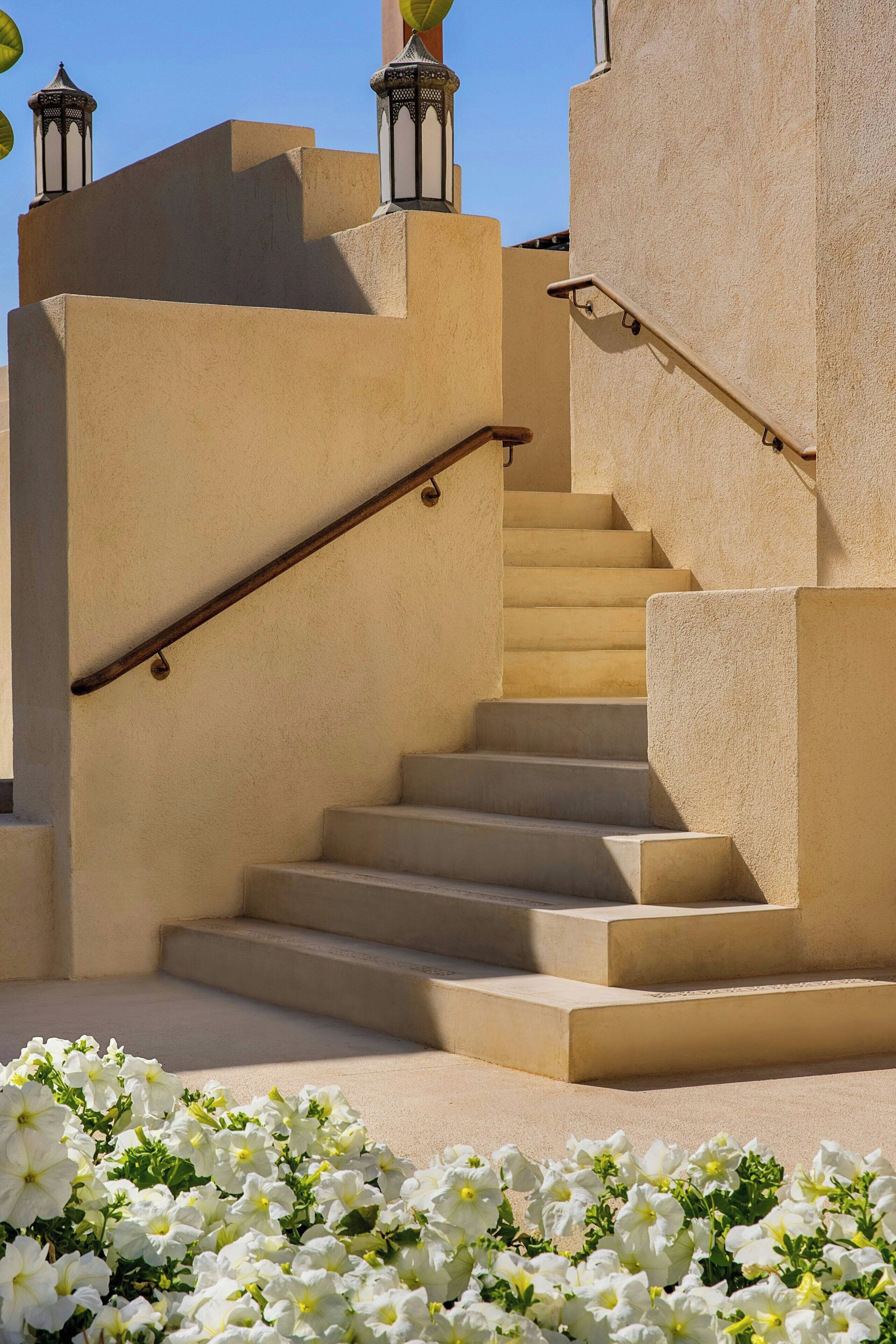 Un escalier beige, doté d’une rampe, mène à un palier agrémenté d’un petit jardin de fleurs blanches.