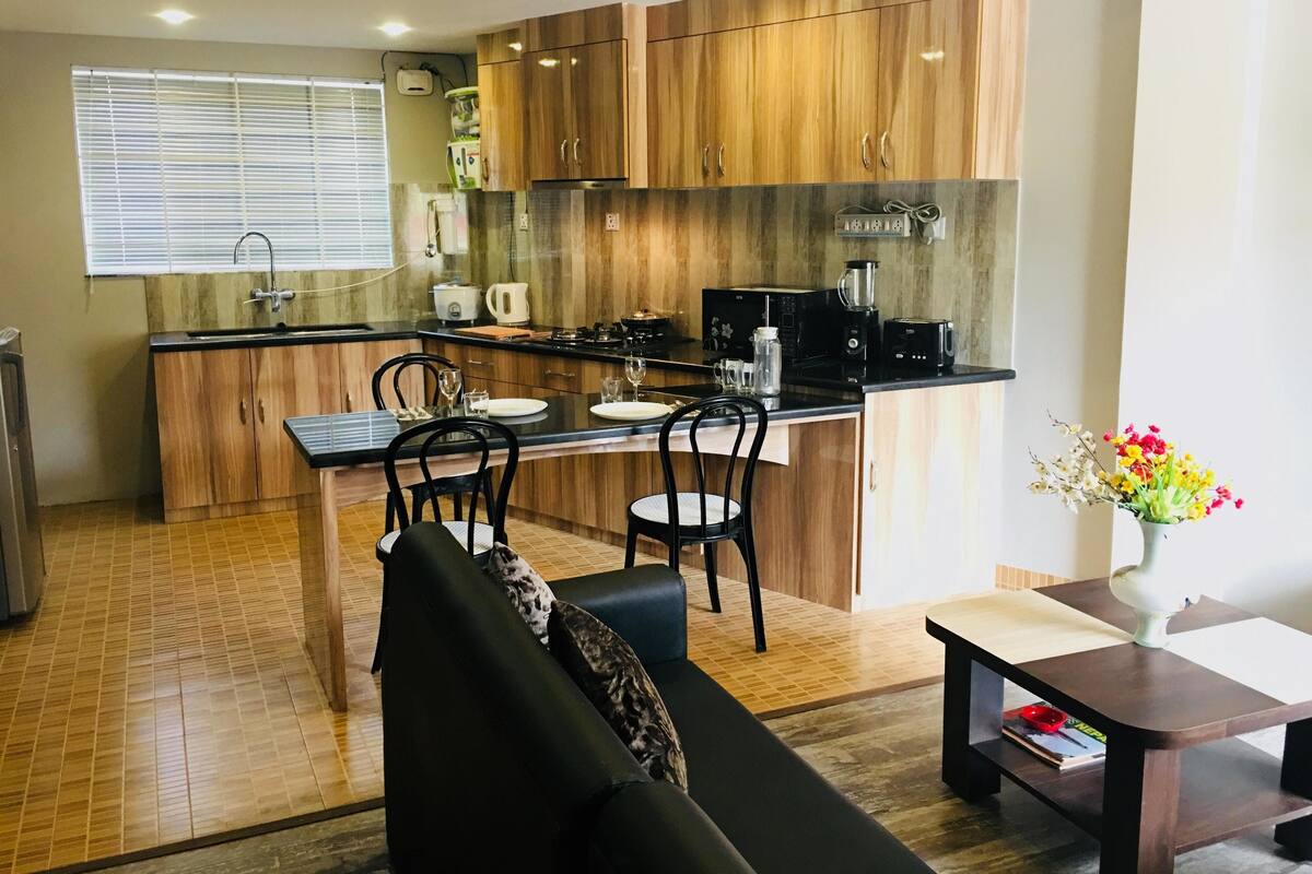 A compact kitchen with wooden cabinets, a black countertop, and a dining area with a sofa and table.