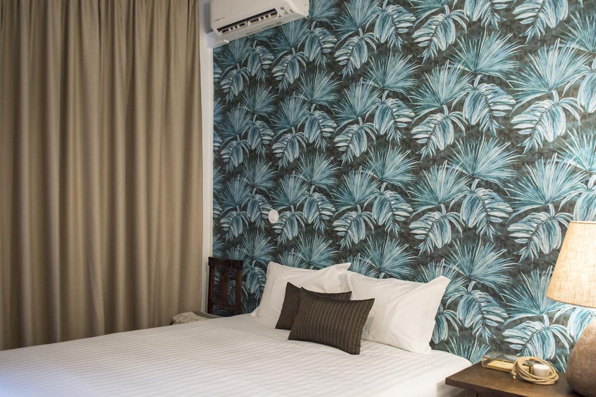 A hotel room with a bed, a nightstand, a lamp, and a wall with a tropical leaf pattern.
