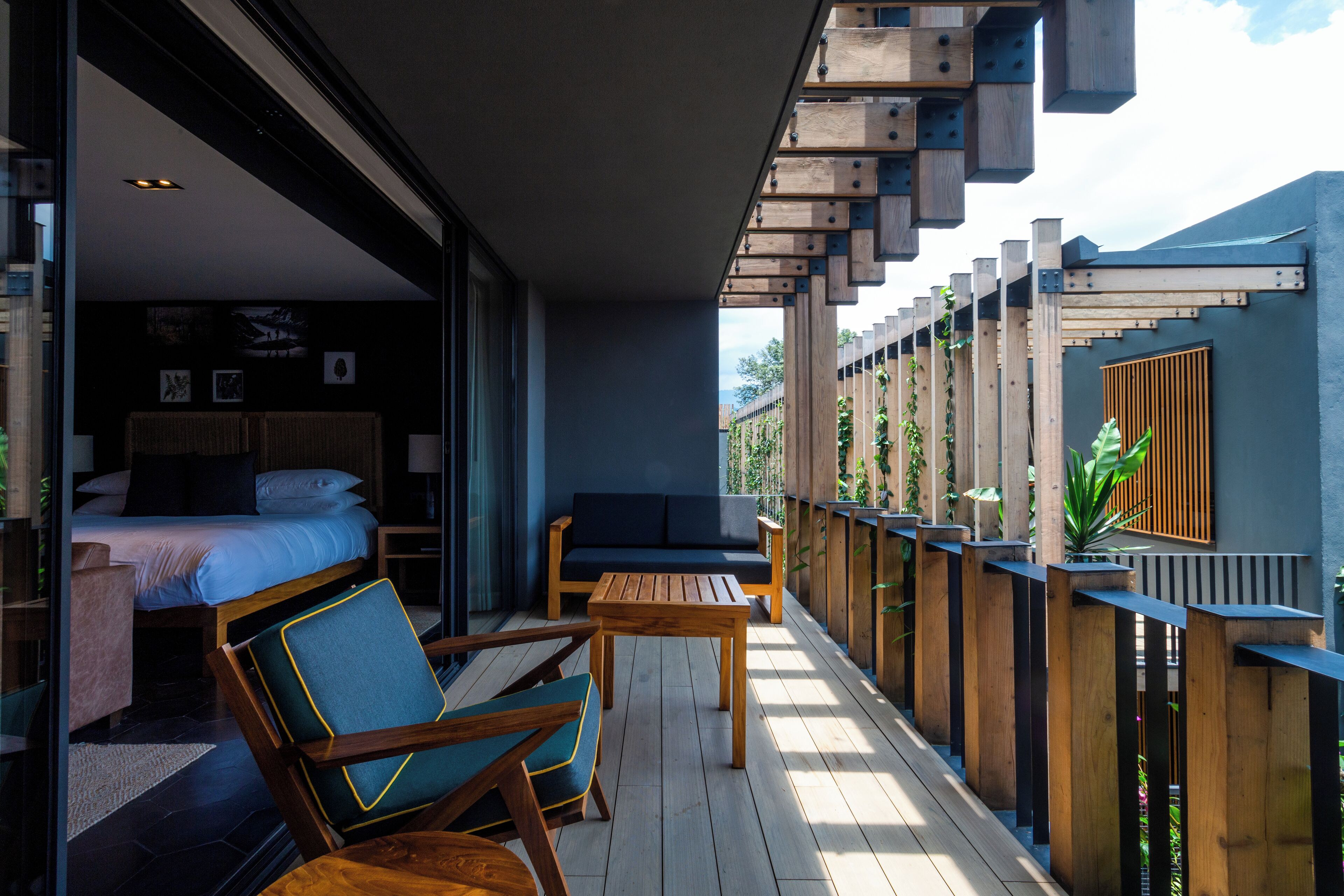 A balcony with wooden furniture, a bed, and a view of greenery.